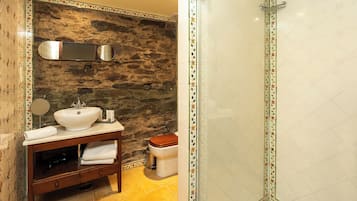 Un baño con pared de piedra, tocador de madera con lavabo e inodoro.