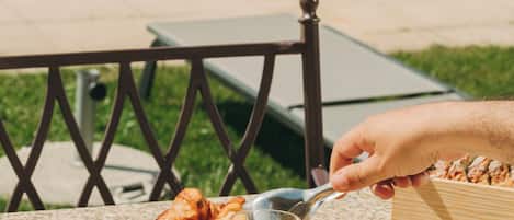A breakfast table with croissants, fruit, and orange juice by a poolside.