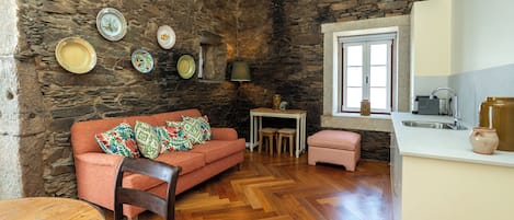 Un área de estar acogedora con una pared de piedra, un piso de madera en espiga, un sofá con cojines coloridos, una mesita y una ventana con vistas.
