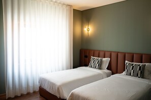 A hotel room with two beds, a large window with sheer curtains, a wall-mounted light fixture, and a brown headboard. - Santo Thyrso Hotel (Santo Tirso)