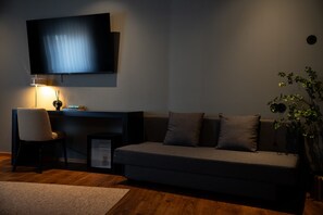 A modern living room with a sofa, a TV mounted on the wall, a desk with a chair, and a small plant. - Santo Thyrso Hotel (Santo Tirso)