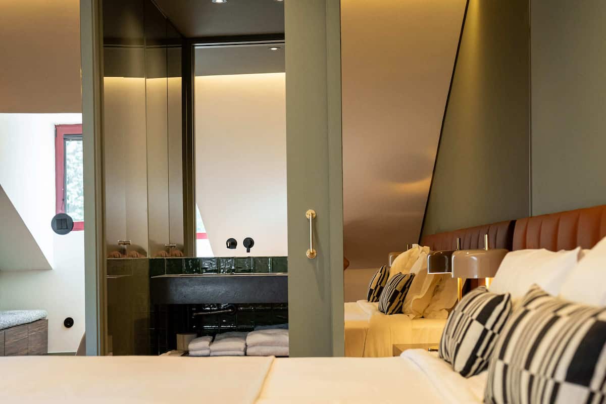 Een moderne hotelkamer met een groot bed, een badkamer met spiegel, en uitzicht op de lucht.