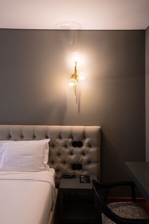 A hotel room with a tufted headboard, a small table with a chair, and a wall-mounted light fixture. - Santo Thyrso Hotel (Santo Tirso)