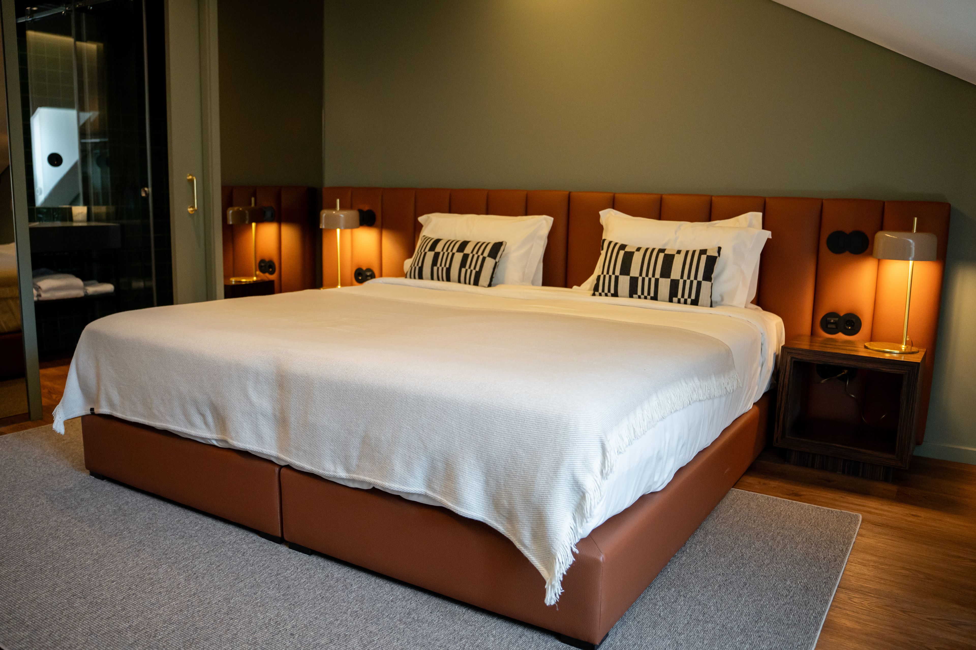 A large bed with a wooden headboard, two bedside lamps, and a neutral-colored rug.