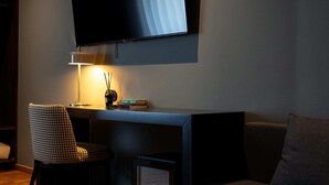 A modern living room with a flat-screen TV mounted on the wall, a desk with a lamp, a chair, and a sofa. - Santo Thyrso Hotel (Santo Tirso)