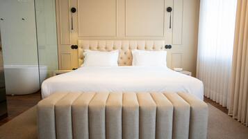 A hotel room with a large bed, a bedside table, a nightstand, a glass shower enclosure, and a large window with curtains.