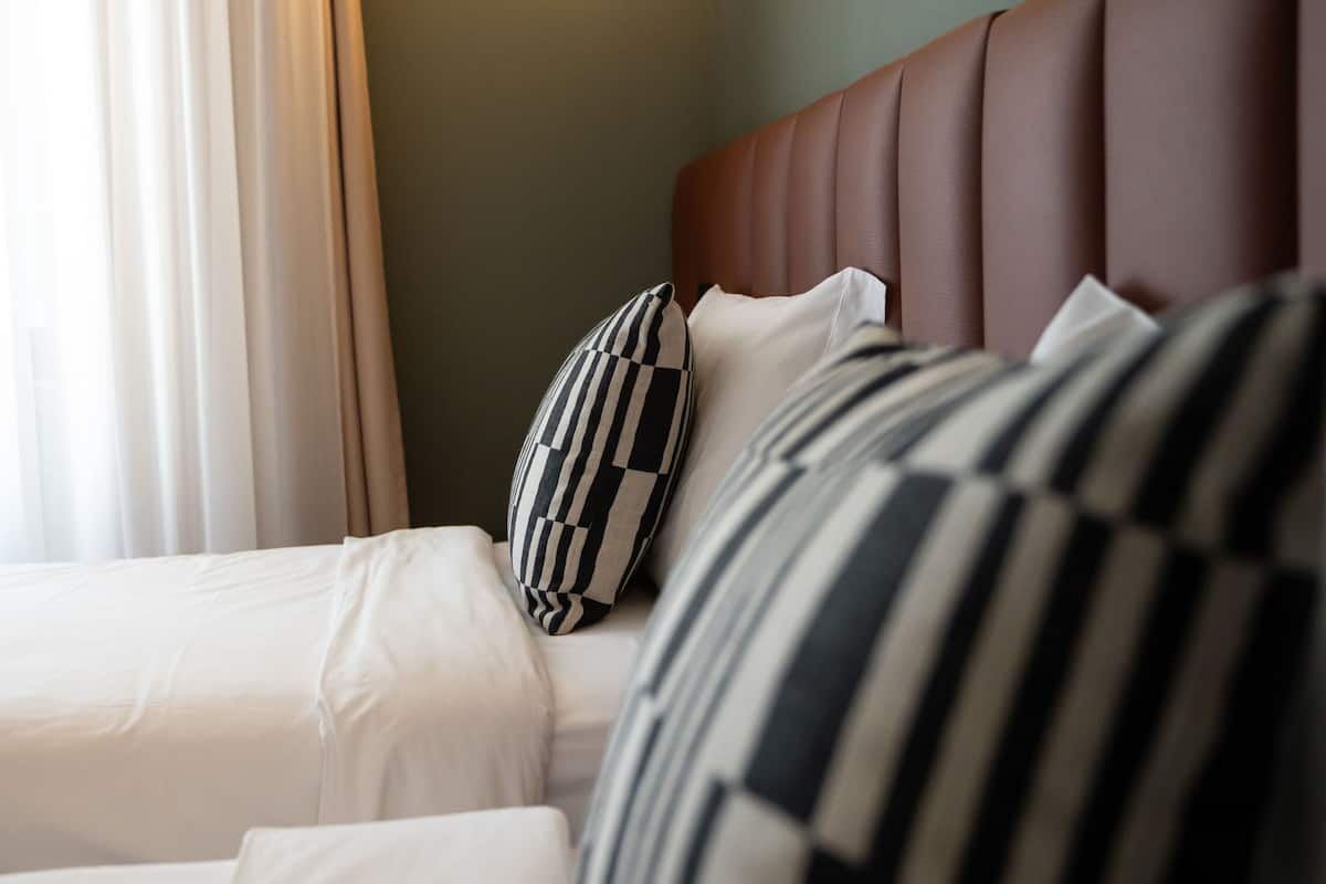 Een hotelkamer met een bed, kussens, een hoofdeinde en een wandlamp.