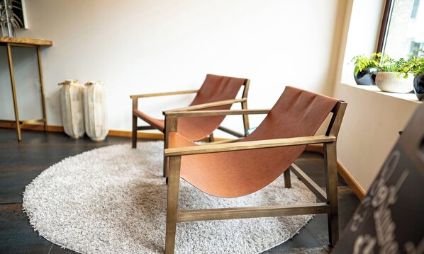 Two leather armchairs with wooden frames on a round rug, a small table with a vase, and potted plants by a window. - Santo Thyrso Hotel (Santo Tirso)