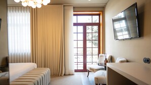 A hotel room with a bed, a seating area, a TV, and a large window with curtains. - Santo Thyrso Hotel (Santo Tirso)