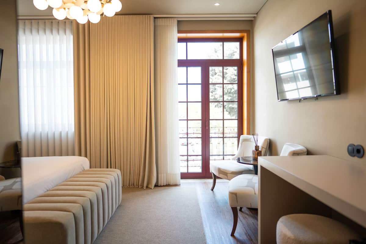 Een hotelkamer met een bed, zithoek, televisie en een groot raam met gordijnen.