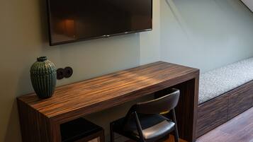 A modern room with a wooden desk, a chair, a television mounted on the wall, and a staircase in the background.