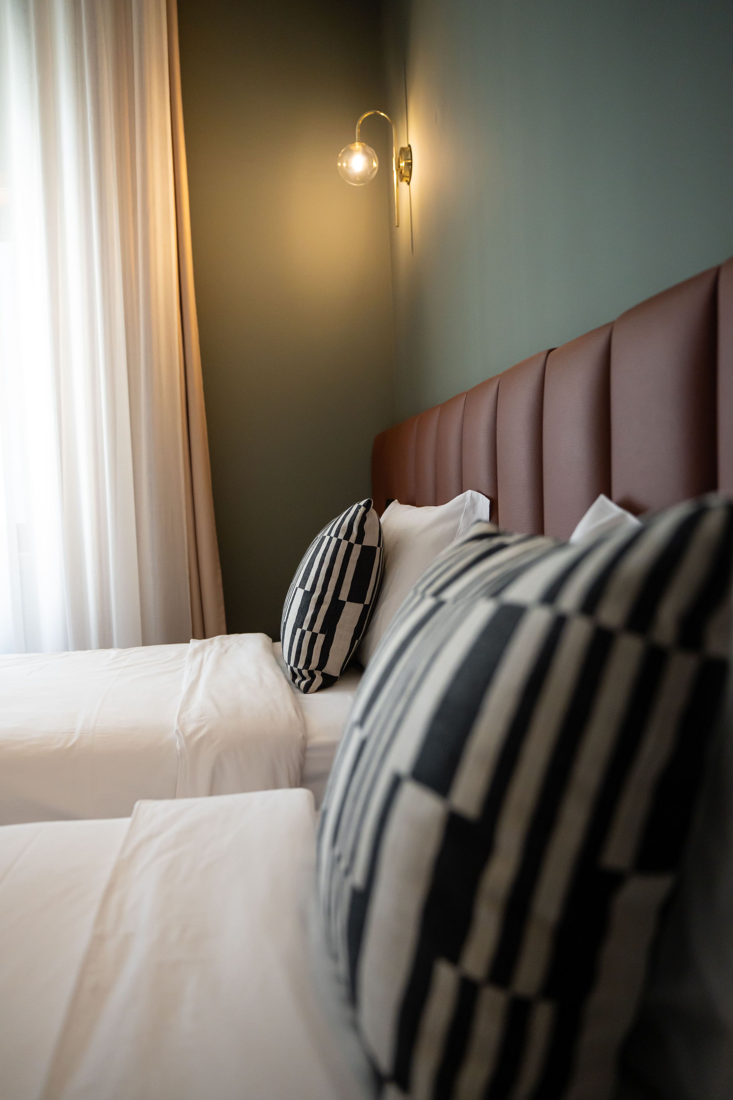 Une chambre d’hôtel avec un lit, des oreillers, une tête de lit et un luminaire fixé au mur.