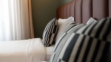 A hotel room with a bed, pillows, a headboard, and a wall-mounted light fixture.