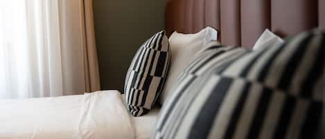 Habitación de hotel con cama, almohadas, cabecero e iluminación unida a la pared.