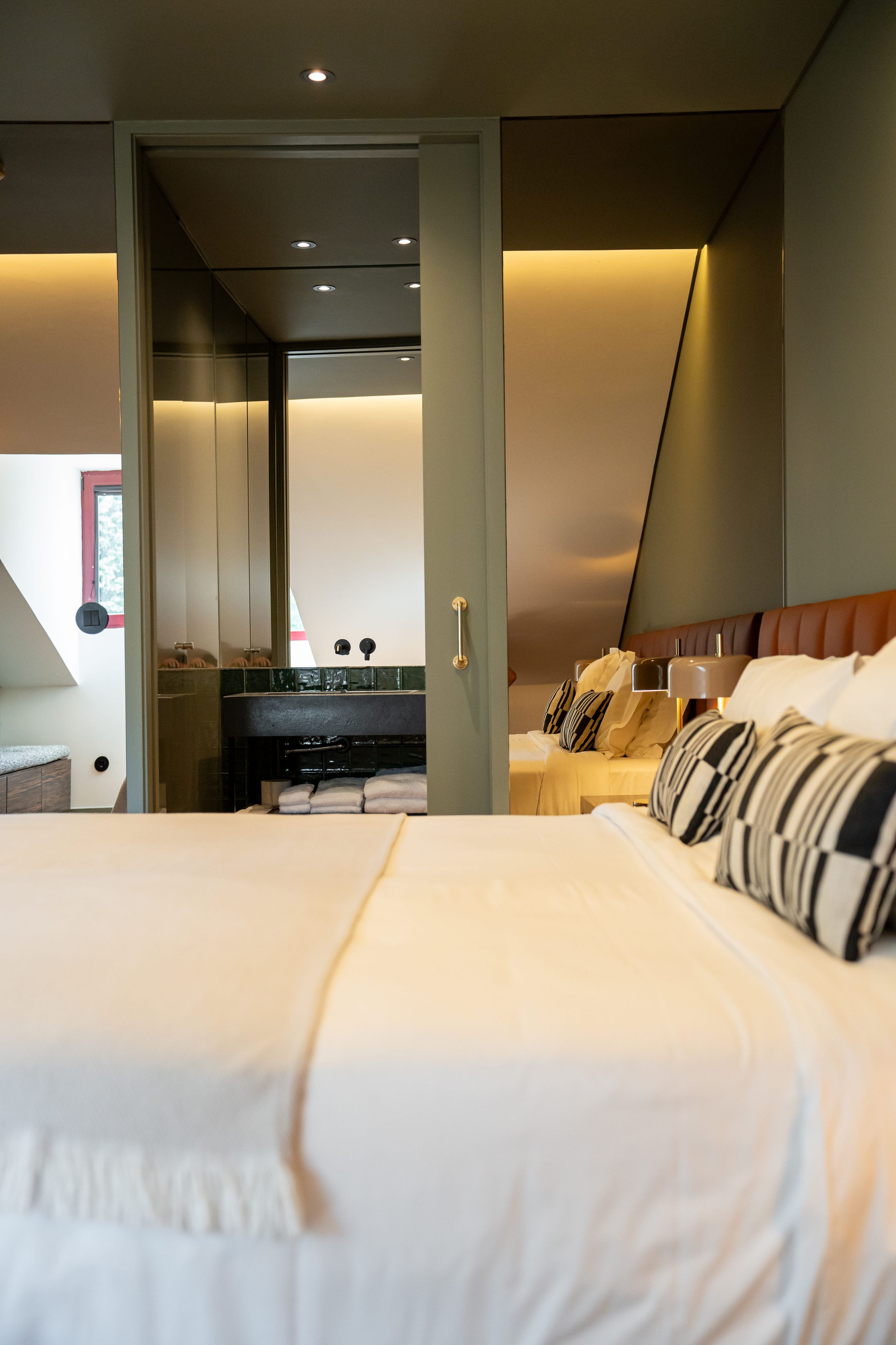 Quarto de hotel moderno com uma cama grande, banheiro com espelho e vista do céu.