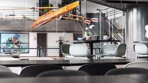 A modern interior with a glass wall, a table with chairs, and a view of an outdoor area with a boat and stairs.