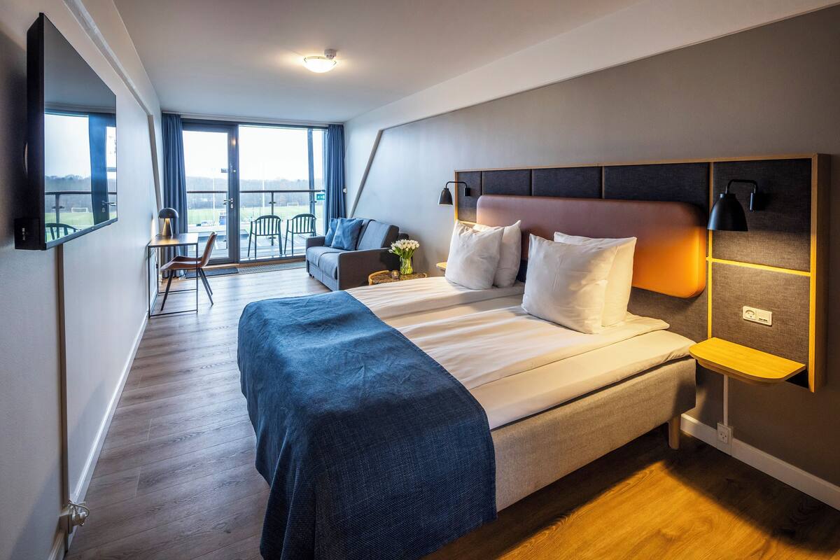 Ein modernes Hotelzimmer mit einem großen Bett, einer Couch, einem Fernseher und einem Balkon mit Blick.
