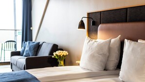 A hotel room with a bed, a nightstand, a lamp, a chair, and a vase with flowers.