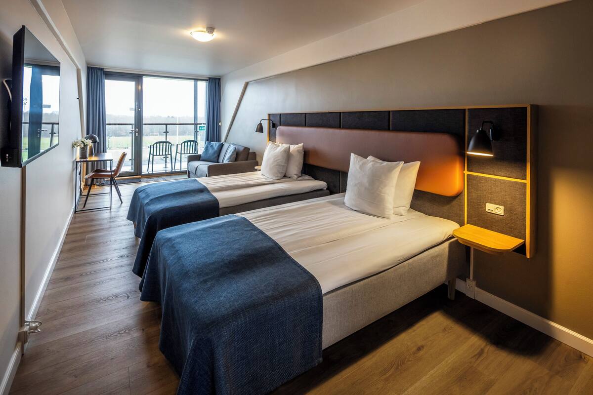 Ein Hotelzimmer mit drei Betten, einem Schreibtisch und einem Stuhl.