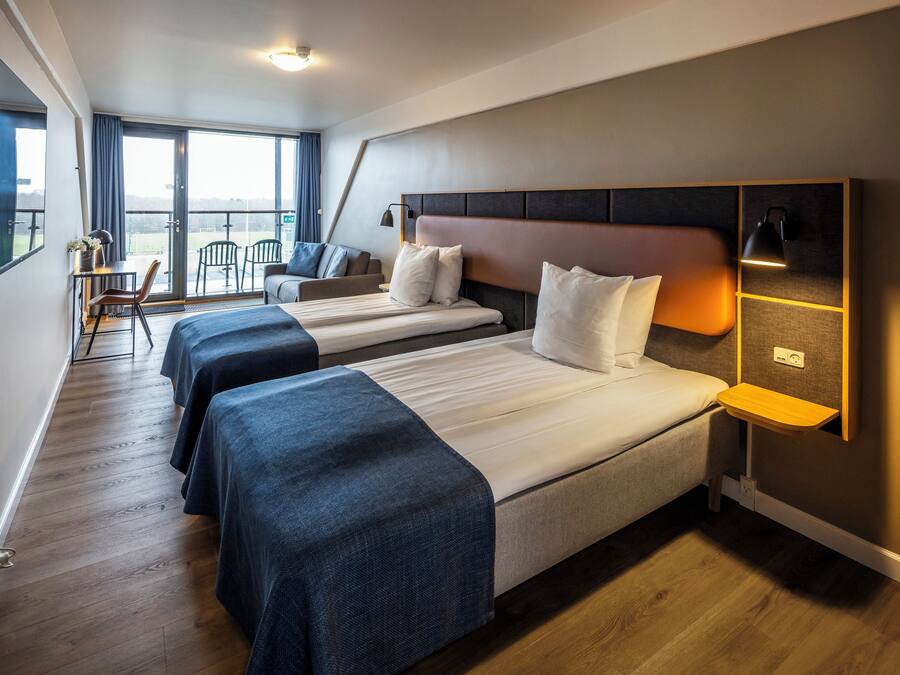 A hotel room with three beds, a desk, and a chair.