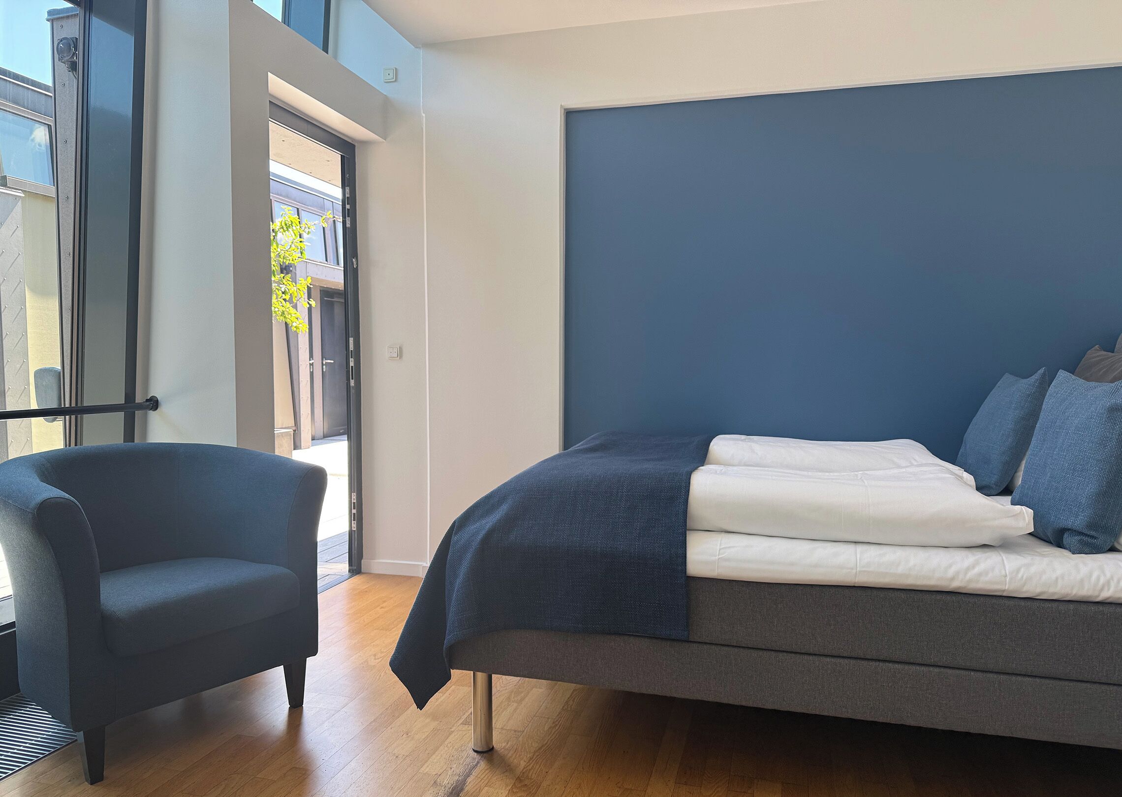 A modern bedroom with a bed, a chair, and a view of the outdoors.