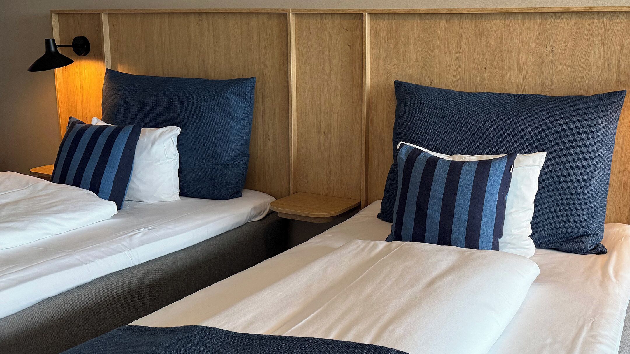 A hotel room with two single beds, each with a pillow and a wooden nightstand.