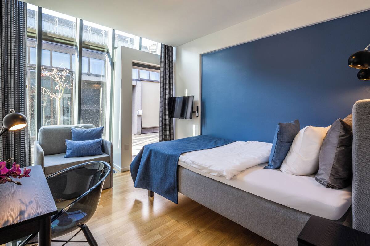 Ein modernes Hotelzimmer mit Bett, einer Sitzecke, einem Schreibtisch und einem Fernseher.
