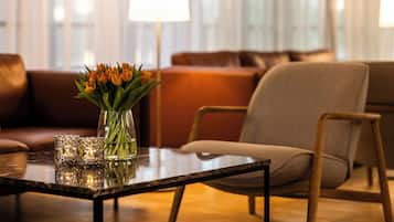A modern living room with a glass vase of flowers on a glass table, a brown leather sofa, and a wooden chair.