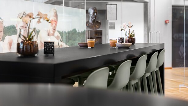 A modern bar area with a long counter, several vases with flowers, and a glass wall displaying a scenic view.