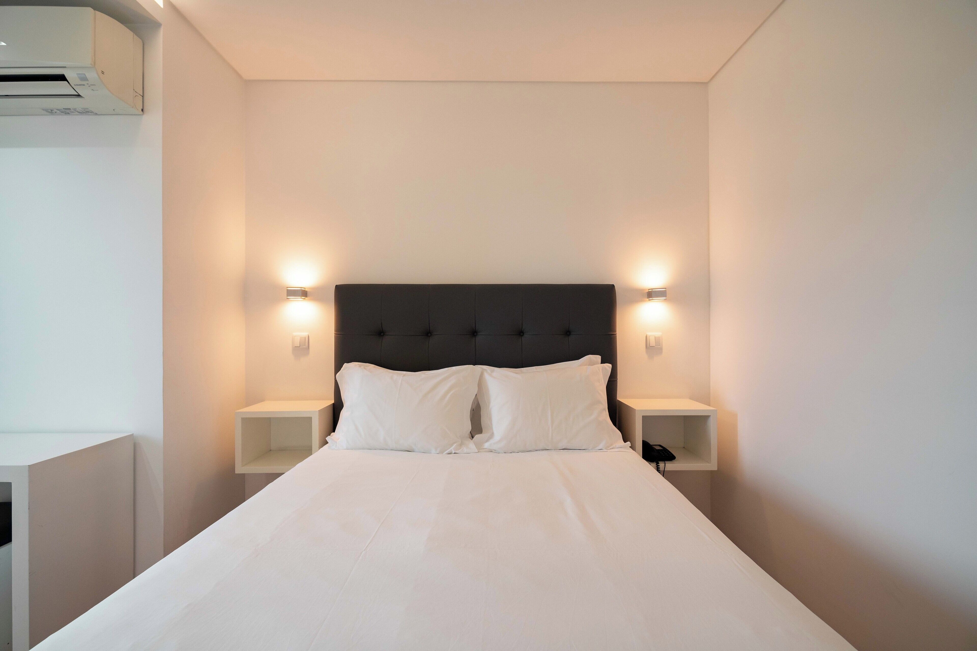 A neatly made bed with white linens, a dark headboard, and two bedside lamps on either side.