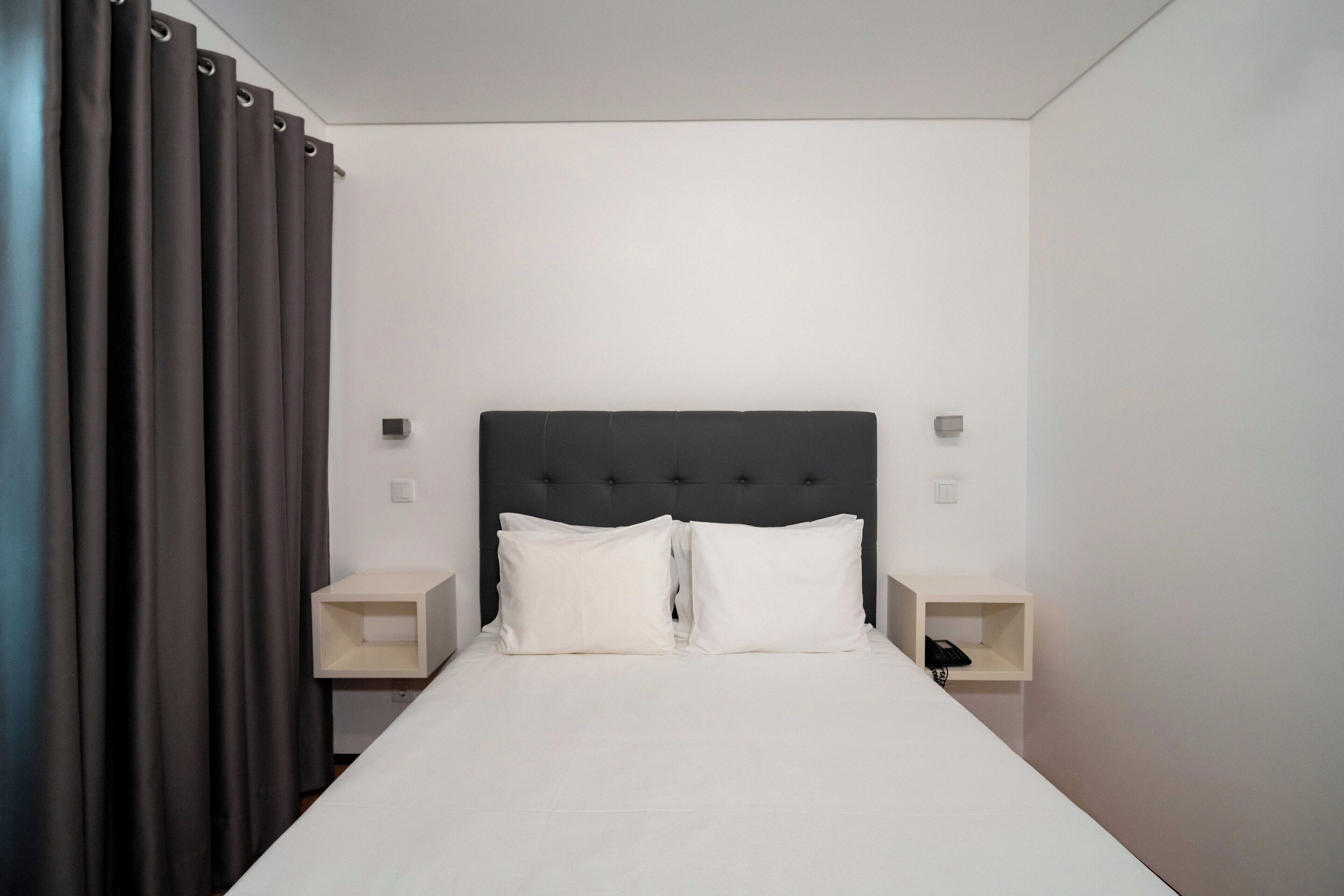 A neatly made bed with white linens, a dark headboard, and two bedside tables with lamps.