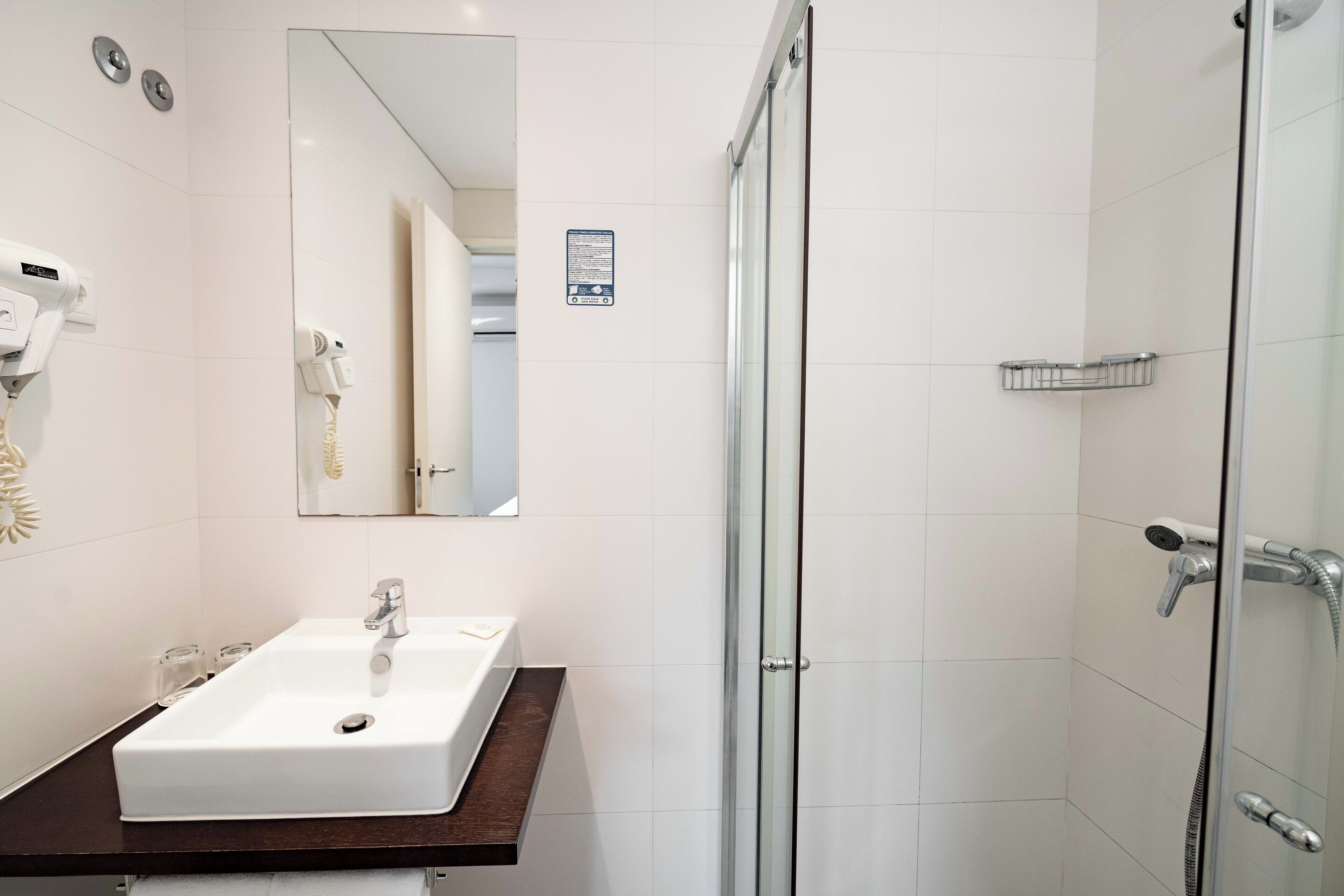Un bagno moderno con lavandino bianco, uno specchio e box doccia in vetro.