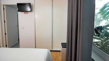 Habitación de hotel con cama, televisor montado en la pared, armario y ventana con cortinas.