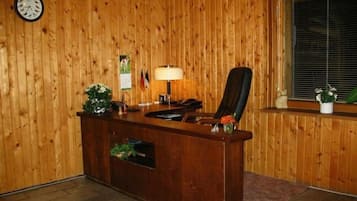 Een kamer met houten lambrisering, een receptiebalie, een klok en een raam met zonwering.