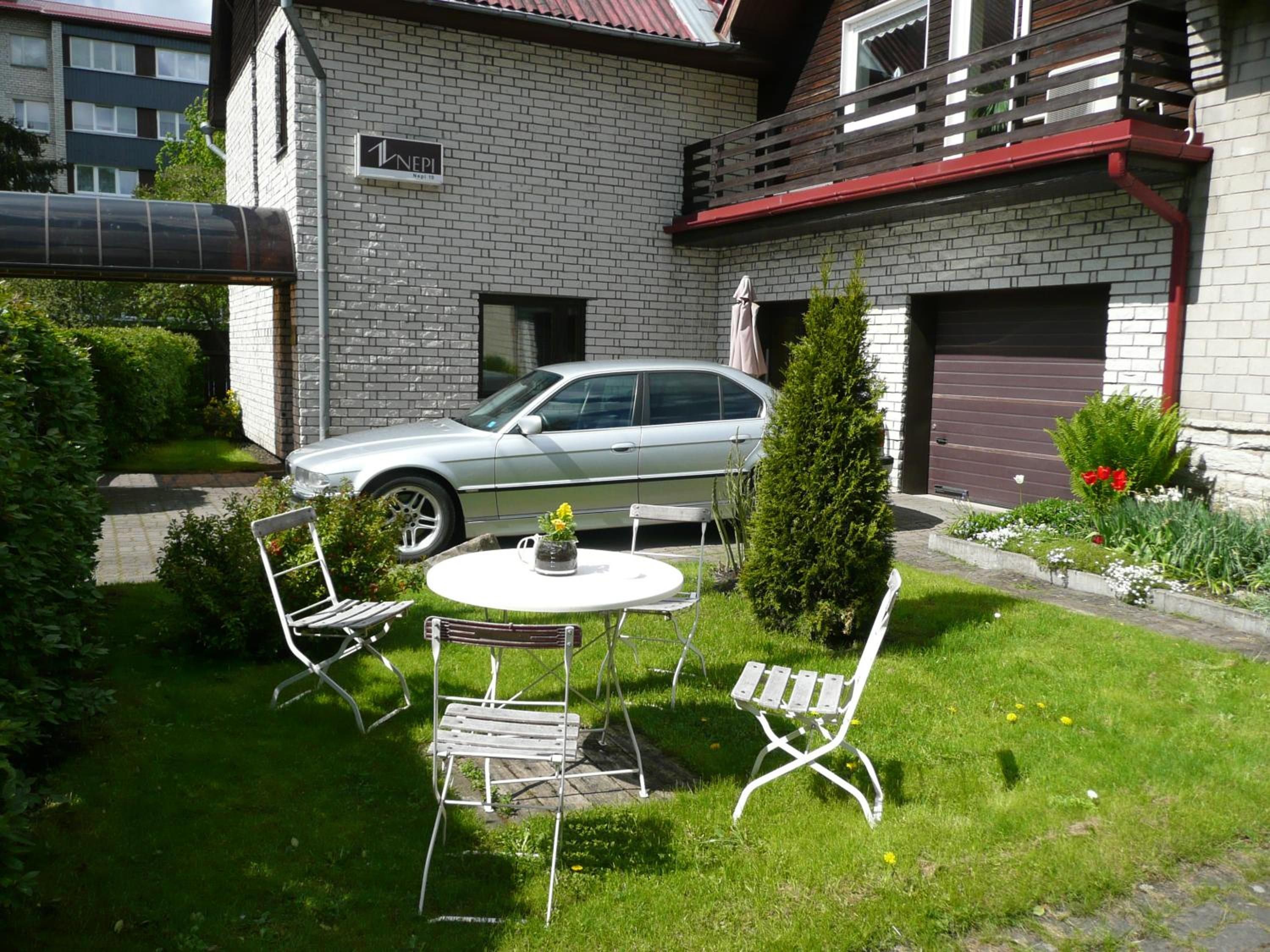 A residential area with a parked car, a small round table with chairs, and a potted plant.