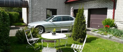 A residential area with a parked car, a small round table with chairs, and a potted plant.