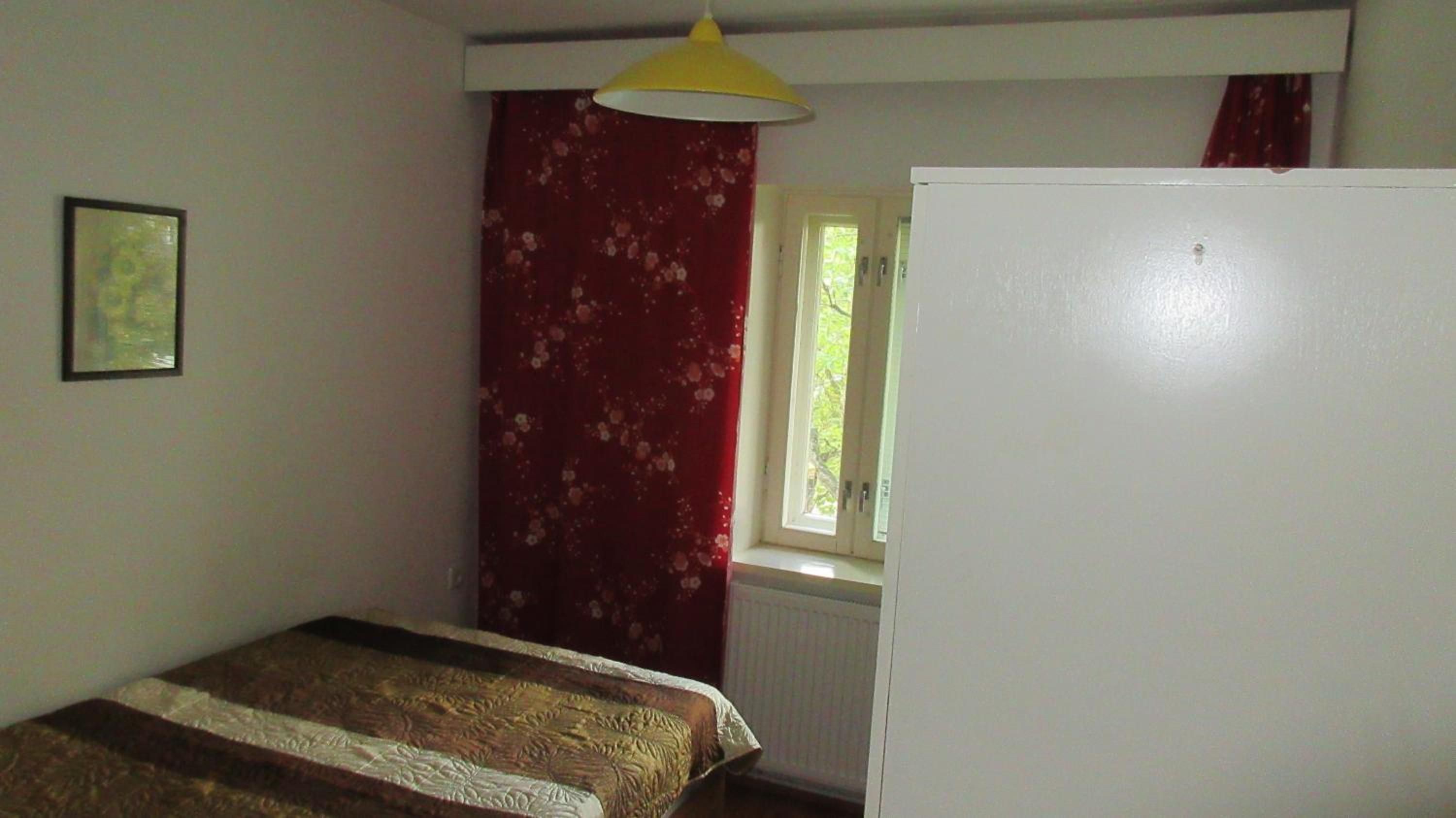 Ein Schlafzimmer mit einem Bett, einem Fenster mit Vorhängen, einem Heizkörper und einer weißen Wand.