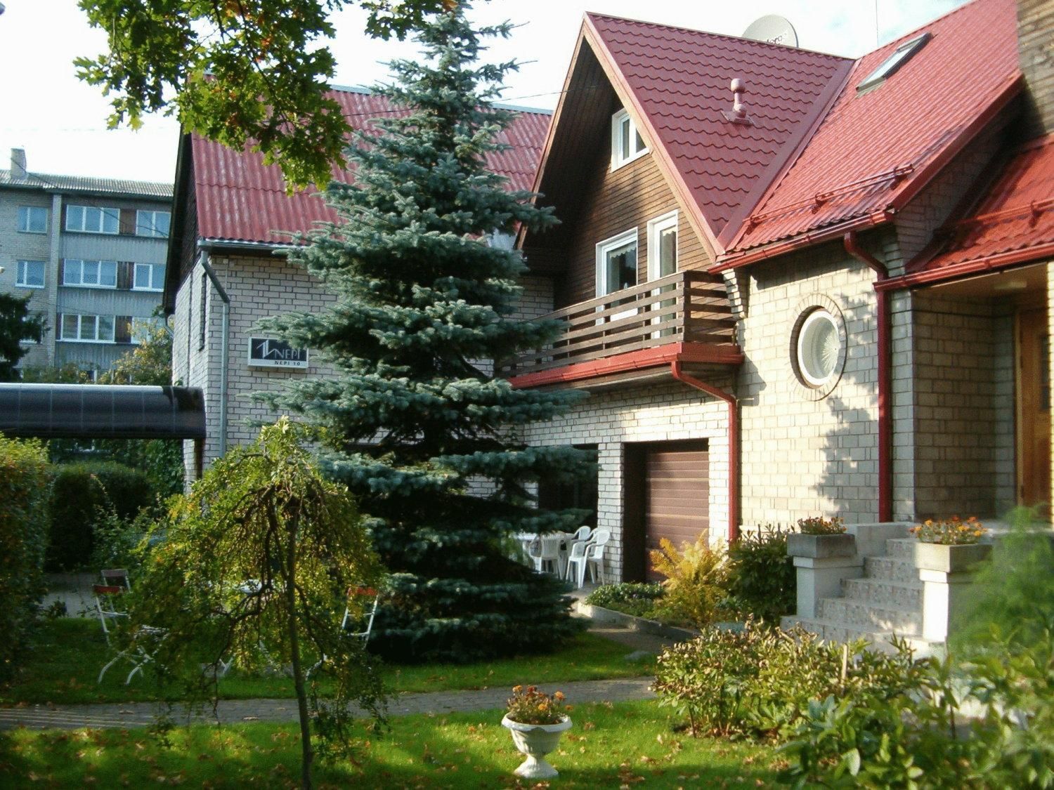 A two-story house with a red roof, a brick exterior, and a large evergreen tree in the front yard.