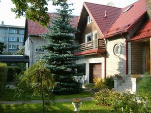 A two-story house with a red roof, a brick exterior, and a large evergreen tree in the front yard. - Nepi Hotell (Tallinn)