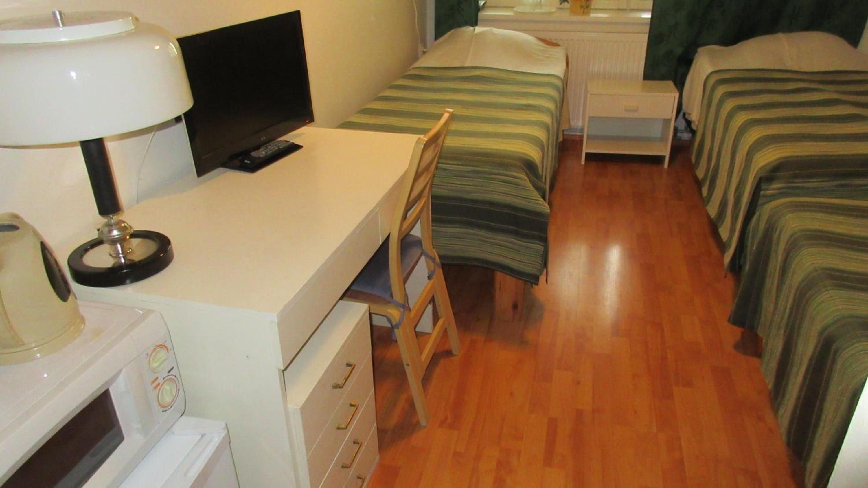 A hotel room with a desk, television, and two beds.