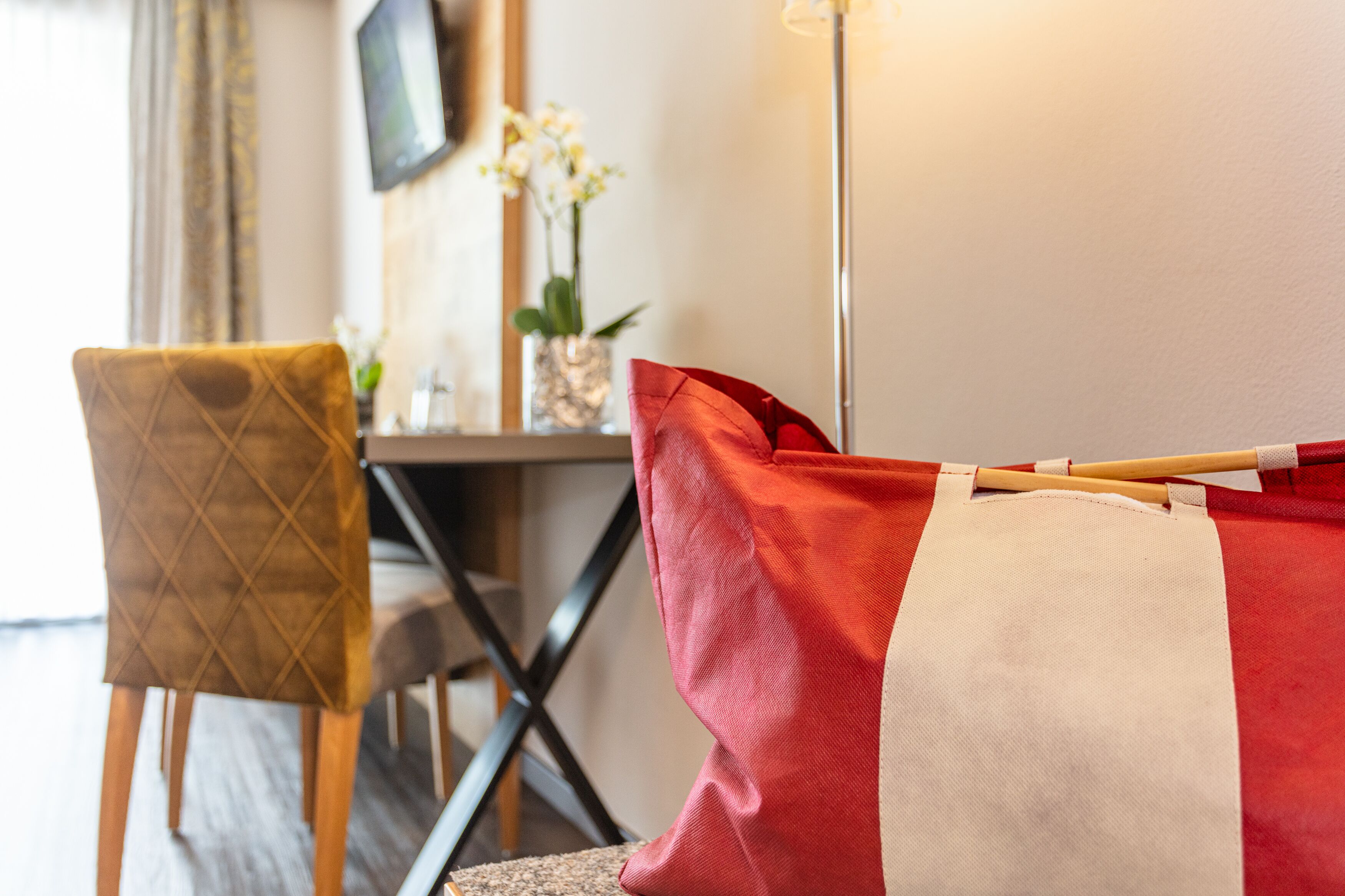 Une pièce comprenant une chaise en bois, un coussin rouge et blanc, une petite table avec un vase de fleurs et un lampadaire.