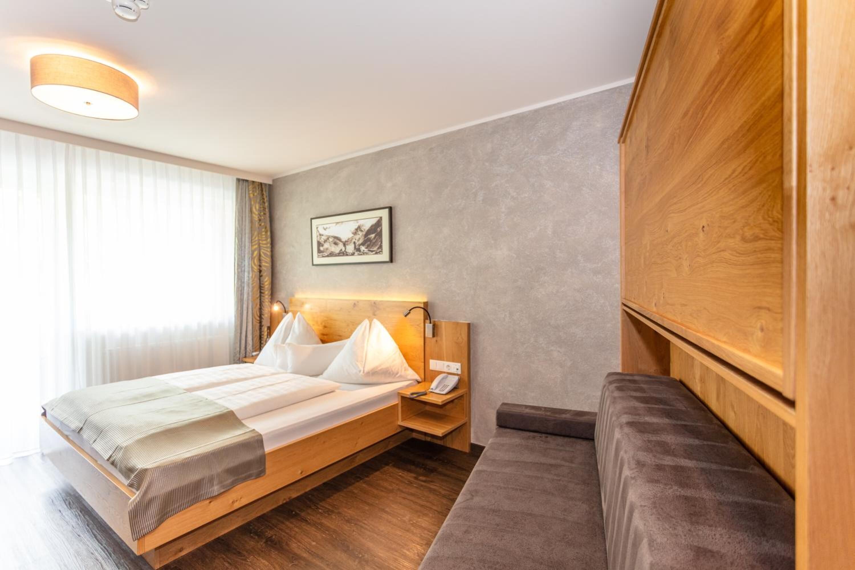 Een hotelkamer met een bed, nachtkastje, lamp en een houten garderobe.