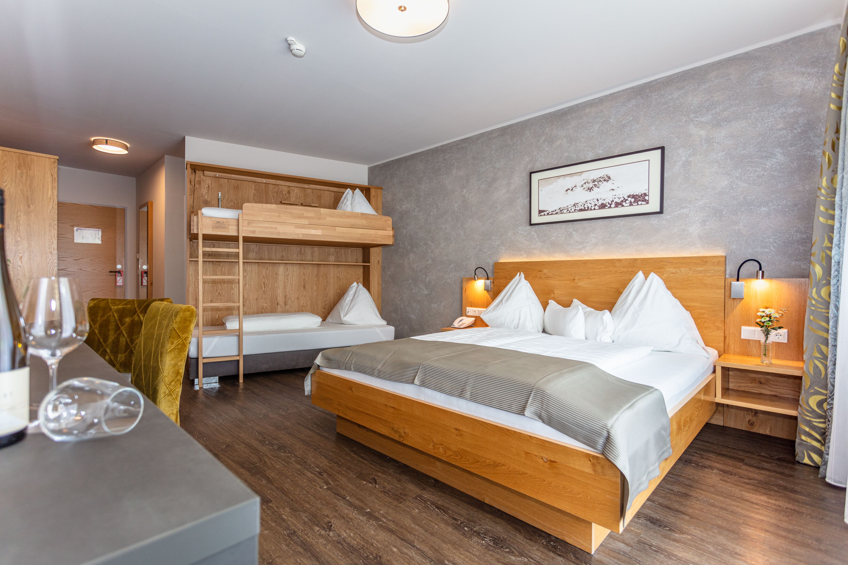Ein Hotelzimmer mit einem hölzernen Bett, einem Stockbett, einem Schreibtisch mit Stuhl und einem Nachttisch mit Lampe.