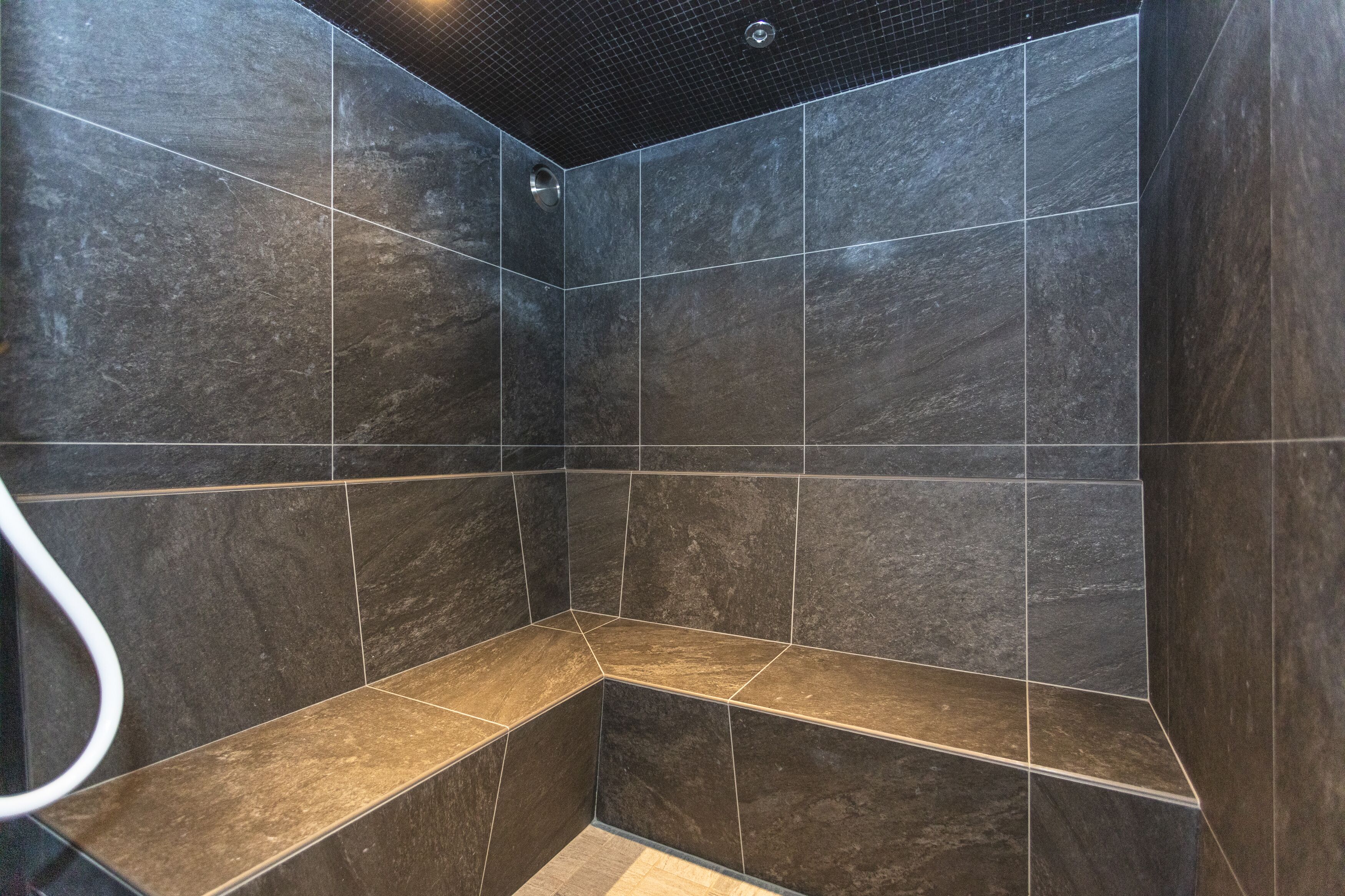 Une douche avec des carreaux de couleur sombre et un banc.
