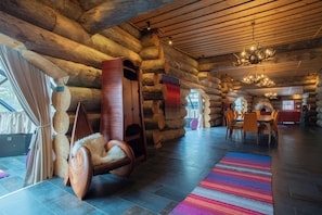 A log cabin interior with a dining area, a wooden rocking chair, and a chandelier.
