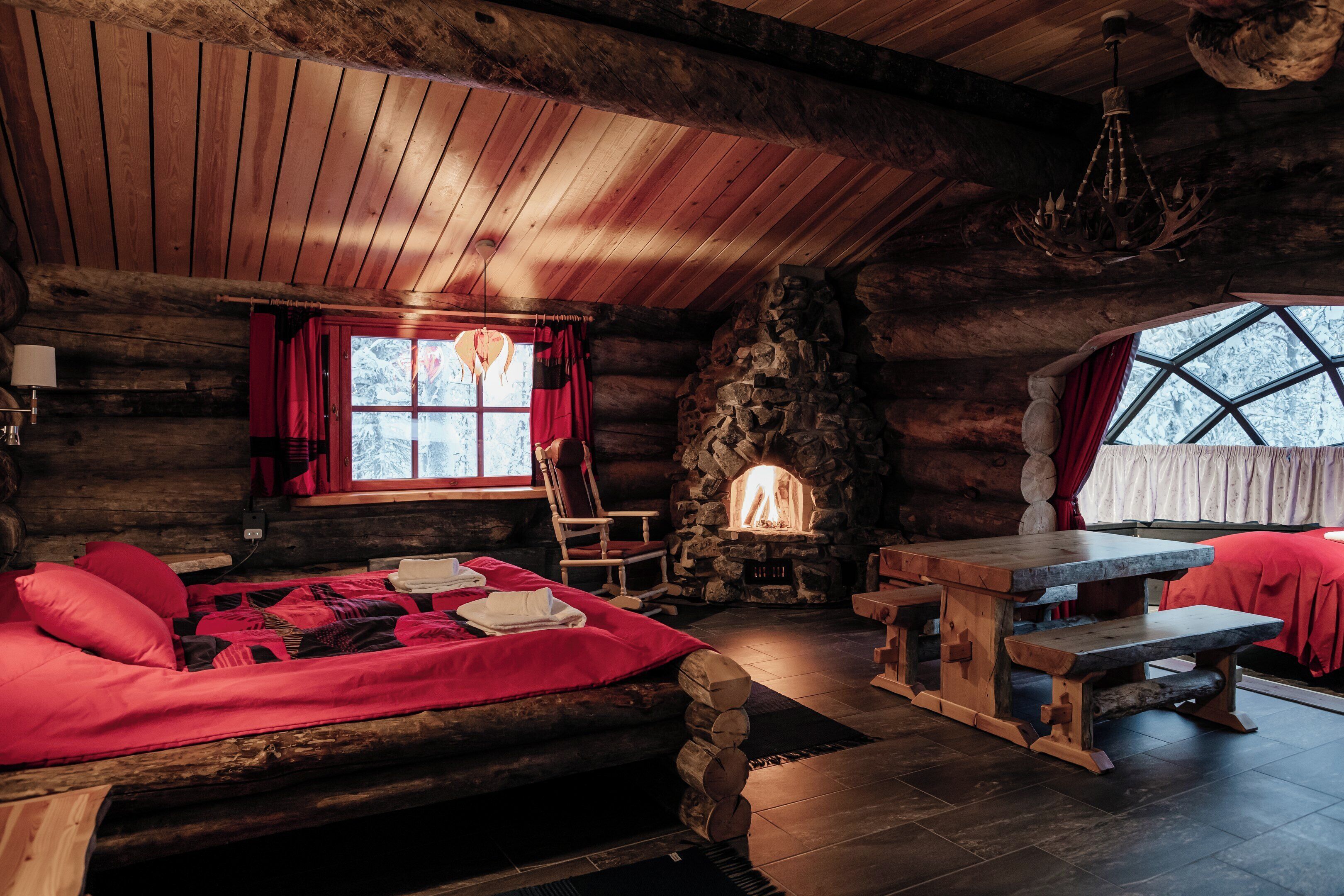 A log cabin interior with a stone fireplace, wooden furniture, and a large window.