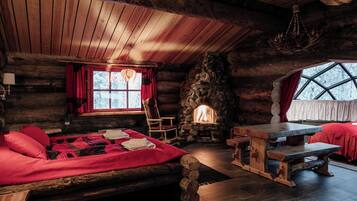 A log cabin interior with a stone fireplace, wooden furniture, and a large window.