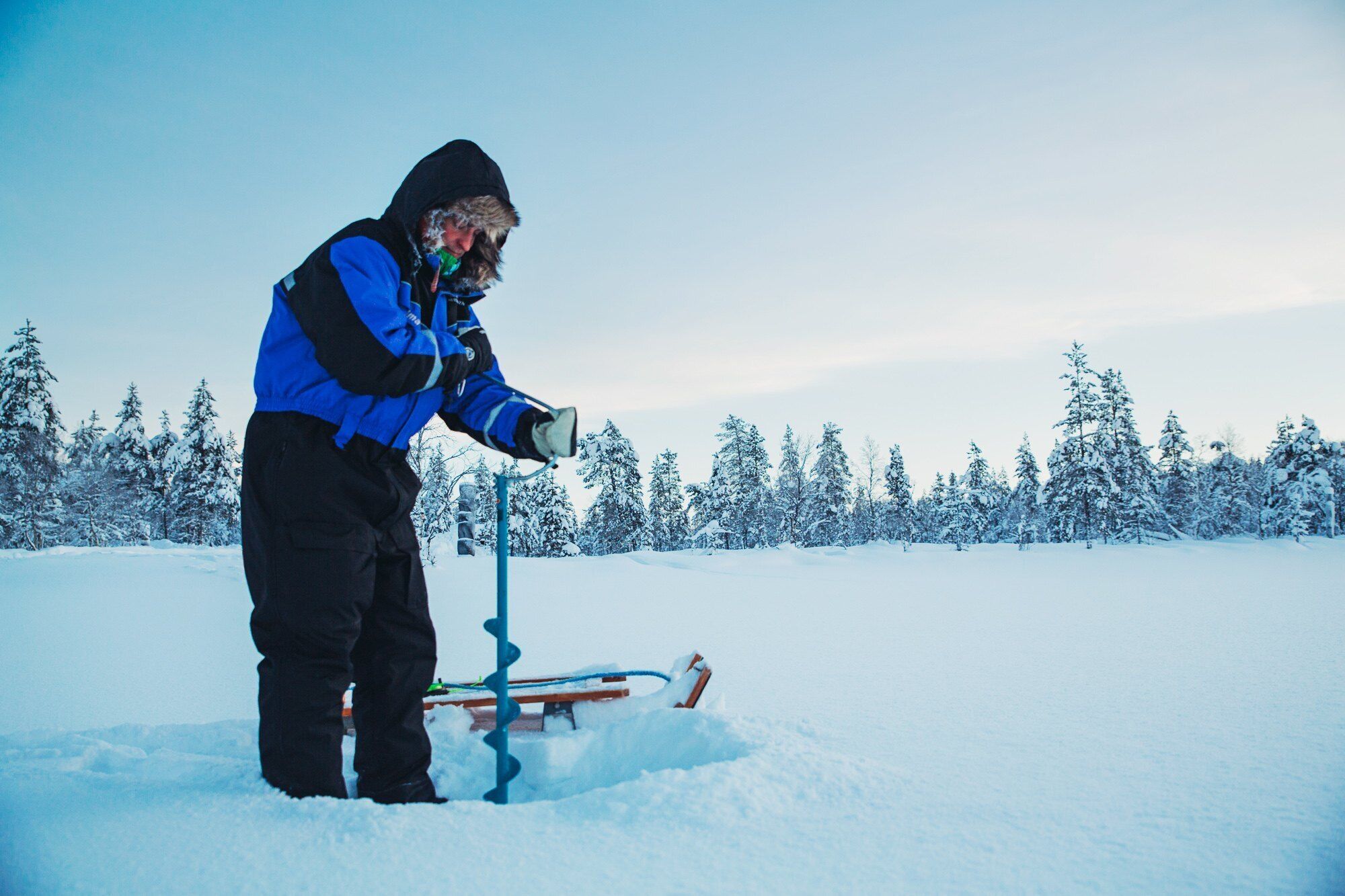 A person in winter clothing standing next to a snow-covered object in a snowy landscape.
