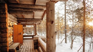 A wooden cabin with a bench and a door, surrounded by a snowy forest. - Kakslauttanen Arctic Resort (Sodankyla)