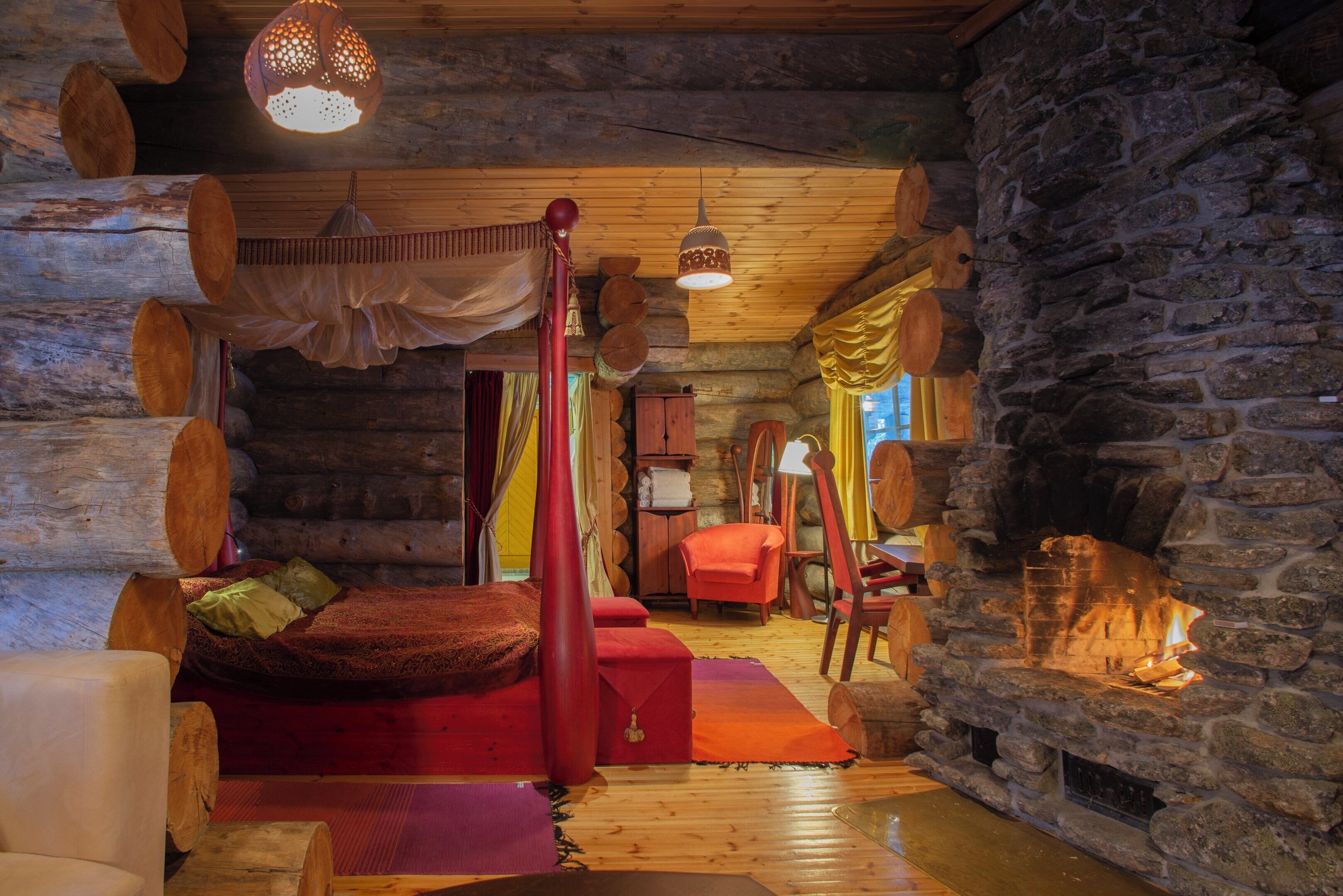 Interior de una cabaña de troncos con chimenea de piedra, una cama con dosel y muebles de madera.